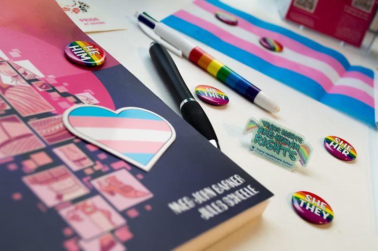A collection of trans-themed pens, badges, stickers, and other items